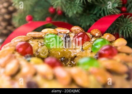 Nahaufnahme von glasierten runden hohlen bunten Weihnachtsfruitcake mit Grüne Kiefernnadeln und rote Bändchendekorationen im Hintergrund Stockfoto