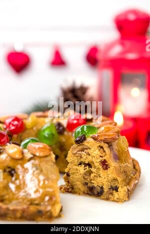 Glasierte bunte Weihnachten Obstkuchen gekrönt mit Mandeln und Glace Kirschen Auf weißem Teller mit Kerzen und Dekorationselementen im Hintergrund Stockfoto