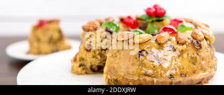 Nahaufnahme von glasierten bunten Weihnachts-Obstkuchen mit Mandeln und Glace Kirschen auf weißem Teller, Panorama-Banner gekrönt Stockfoto