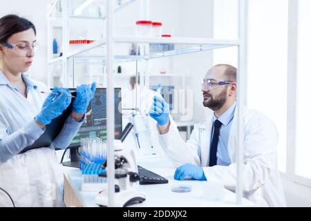 Junger Wissenschaftler, der nachdenklich an der chemischen Lösung in Reagenzgläsern sucht. Team von chemischen Chemikern, die im Labor für sterile Mikrobiologie zusammenarbeiten und forschen. Stockfoto