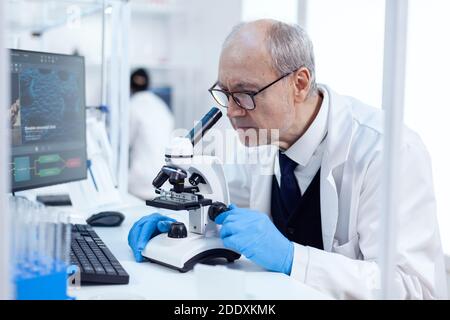 Leitender Mann, der wissenschaftliche Untersuchungen durch das Mikroskop durchführt. Chemiker Forscher im sterilen Labor macht Experimente für die medizinische Industrie mit moderner Technologie. Stockfoto