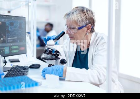 Leitender Wissenschaftler, der wissenschaftliche Experimente mit dem Mikroskop durchführt. Ältere Forscher, die wissenschaftliche Forschung in einem sterilen Labor mit einer modernen Technologie. Stockfoto