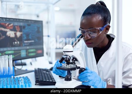 Medizinischer Forscher mit afrikanischer Ethnizität unter Verwendung des Mikroskops, der Untersuchung macht und Probe auswertet. Schwarzer Gesundheitswissenschaftler im biochemischen Labor, der sterile Geräte trägt. Stockfoto