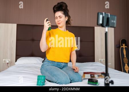 Soziale Medien und Vlogging. Eine schöne weibliche Vlogger Streaming Live-Video auf Smartphone sitzen auf dem Bett und testen eine neue Kosmetik an sich. Stockfoto