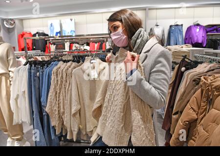 Themenbild SCHWARZ FREITAG am 26. November 2020. Eine junge Frau mit Gesichtsmaske, Maske schaut auf Textilien, Kleidungsstücke in einem Modegeschäft in Zeiten der Corona-Pandemie, Sperrung, Abschaltung, Inzidenzwert. MODELL FREIGEGEBEN! Weltweite Nutzung Stockfoto