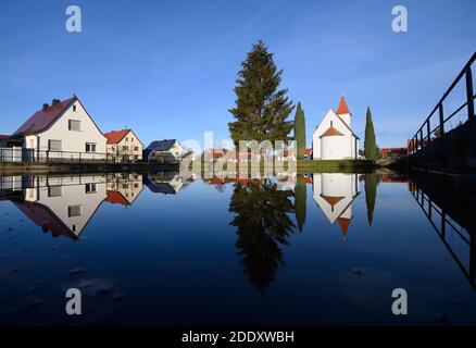 Saalau, Deutschland. November 2020. Die Kapelle auf dem Dorfplatz in Saalau, Bäume und Häuser spiegeln sich in einem Teich. Das Dorf im Norden des Kreises Bautzen in Ostsachsen gehört seit 1994 zur Stadt Wittichenau. Es liegt in der oberLausitzer Heide- und Teichlandschaft und ist Teil des sorbischen Siedlungsgebietes. Quelle: Robert Michael/dpa-Zentralbild/ZB/dpa/Alamy Live News Stockfoto