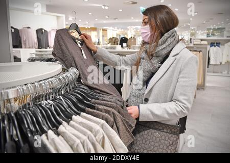 Themenbild SCHWARZ FREITAG am 26. November 2020. Eine junge Frau mit Gesichtsmaske, Maske schaut auf Textilien, Kleidungsstücke in einem Modegeschäft in Zeiten der Corona-Pandemie, Sperrung, Abschaltung, Inzidenzwert. MODELL FREIGEGEBEN! Weltweite Nutzung Stockfoto