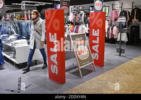 Themenbild SCHWARZ FREITAG am 26. November 2020. Eine junge Frau mit Gesichtsmaske, Maske kommt aus einem Modehaus. Daneben sind Schilder und Displays VERKAUF, RABATT. Pandemie, Sperrung, Abschaltung, Inzidenzwert. MODELL FREIGEGEBEN! Weltweite Nutzung Stockfoto