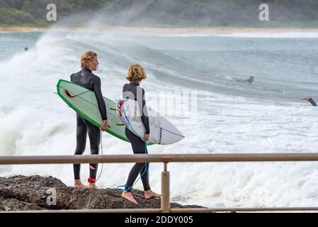 Zwei junge männliche Surfbrettfahrer beobachten sorgfältig, wie sie sich vorbereiten Um in das Wasser von den Felsen bei Schwarz zu springen Head Beach Ocean Pool in Australien Stockfoto