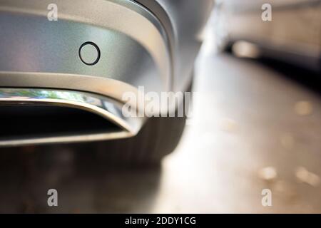 Selektiver Fokus auf den Parksensor des hinteren Stoßfängers in der Nähe des Auspuffrohrs Auf der Rückseite des luxuriösen Auto Stoßstange Nahaufnahme in der Nähe von anderen Auto auf Licht verschwommen mit Sonne Stockfoto