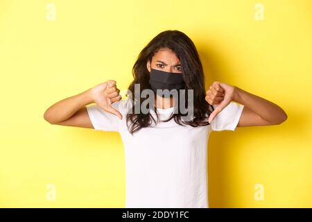 Konzept von covid-19, sozialer Distanzierung und Lebensstil. Bild der verstörten afroamerikanischen Protesterin, trägt schwarze Gesichtsmaske, zeigt Daumen nach unten Stockfoto