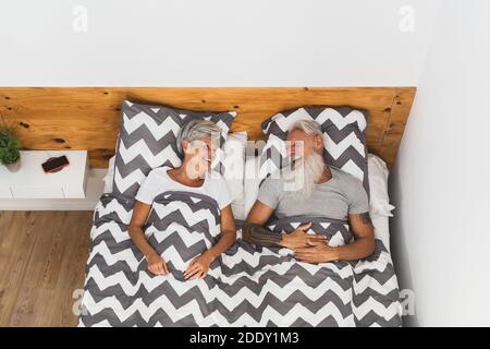 Glückliches Seniorenpaar lächelt zusammen im Bett - Hipster reif Leute, die eine lustige Schlafzeit haben - älterer Lebensstil und Liebe Beziehungskonzept Stockfoto