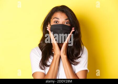 Konzept von Coronavirus, Pandemie und Lebensstil. Close-up von afroamerikaner Mädchen in schwarzen Gesichtsmaske erstaunt, Blick gefragt, etwas ehrfürchtiges Stockfoto