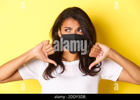 Konzept von covid-19, sozialer Distanzierung und Lebensstil. Nahaufnahme von widerstrebenden und unzufrieden afroamerikanischen Mädchen, trägt schwarze Gesichtsmaske, zeigen Stockfoto