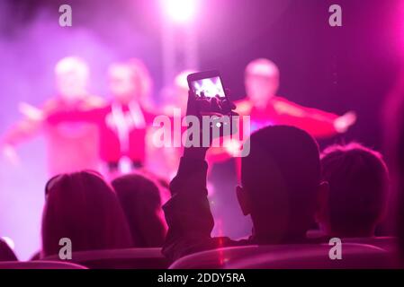 Ein Mann aus einem Konzertsaal schießt eine Bühnenperformance auf einem Smartphone. Stockfoto