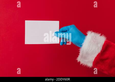 Santa Hände tragen blaue Schutzhandschuhe mit einem Rohling Karte Stockfoto