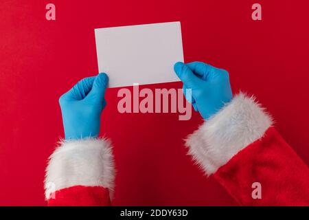 Santa Hände tragen blaue Schutzhandschuhe mit einem Rohling Karte Stockfoto