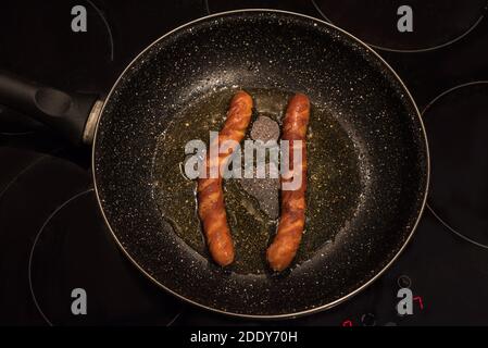 Würstchen in der Bratpfanne. Würstchen in einer gusseisernen Pfanne Nahaufnahme, Frühstück, zwei Würstchen werden auf dem Herd gebraten. Stockfoto