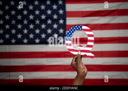 Hände mit Q-Alphabet mit US-Flagge als Hintergrund mit Copy Space - Konzept QAnon oder Q Anon tiefen Zustand Verschwörungstheorie Stockfoto