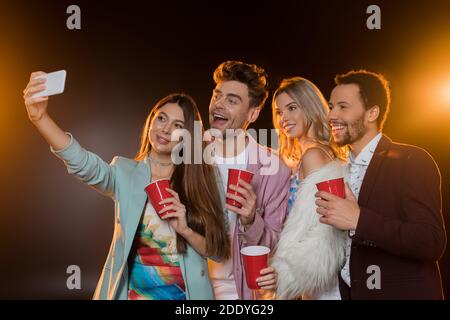 Gruppe von glücklichen multikulturellen Freunden, die Selfie machen, während sie Plastik halten Tassen auf schwarz Stockfoto