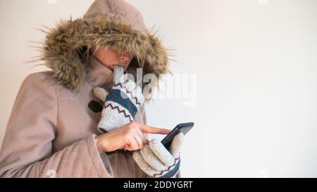 Gefrorene Frau in warmen Mantel mit einer Kapuze über dem Kopf gekleidet verwendet ein Smartphone. Stockfoto