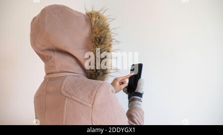 Eine Frau, die von hinten in einer Kapuzenjacke fotografiert wird, benutzt ein Telefon. Stockfoto