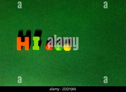 Bunte Holzbuchstaben Textwort Hallo Inschrift mit Ellipse Perlen auf grünem Bastelpapier Hintergrund, freundliche Begrüßung Stockfoto