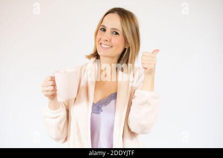 Lächelnd hübsche junge Frau im Schlafkleid zeigt Daumen nach oben Isoliert auf weißem Hintergrund Stockfoto