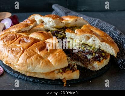 Delilicous Party Snack mit gefülltem amerikanischen Fladenbrot mit langsam gekochtem gebratenem Rindfleisch, karamellisierten Zwiebeln, Käse und Gurken auf dunklem Teller serviert Stockfoto