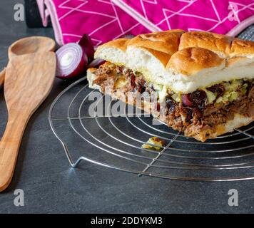 Hausgemachte gefüllte Fladenbrot mit Roastbeef aus einem langsamen Herd, Käse, karamalisierte rote Zwiebeln und Gurken auf einem Küchentisch serviert Stockfoto