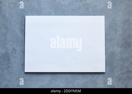 Weißes Blatt auf grauem Betongrund. Speicherplatz kopieren. Leeres Modell auf neutralem Hintergrund. Draufsicht, flach liegend. Stockfoto