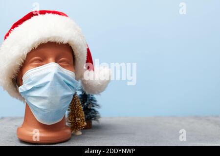 Covid 19, medizinische Maske auf einer Schaufensterpuppe und weihnachtshut 2021 auf blauem Hintergrund, Banner, Kopierraum Stockfoto