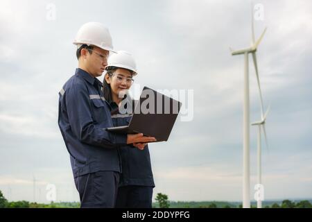 Asiatische Mann und Frau Inspektionsingenieure Vorbereitung und Fortschrittskontrolle mit Laptop einer Windenergieanlage mit Sicherheit in Windpark in Thailand. Stockfoto