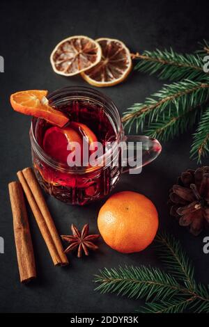 Heißer Glühwein in Glas Tasse auf dunklem Hintergrund. Warmes Weihnachtsgetränk mit Gewürzen und Früchten. Stockfoto