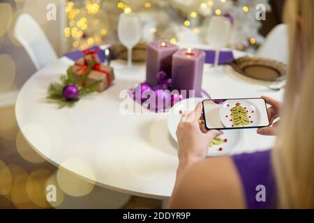 Mädchen Hand macht Bilder von Weihnachtstisch. weihnachten Tischdekoration. Kiwi und Granatapfel in Form eines weihnachtsbaums auf einem Teller. High qu Stockfoto