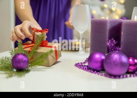 Mädchen macht Weihnachten Tischdekoration mit Geschenken und lila Kerzen.hoch Qualität Stockfoto