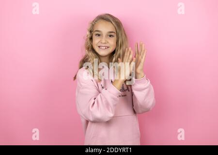 Junge schöne Kind Mädchen stehen über isoliert rosa Hintergrund klatschen und applaudieren glücklich und fröhlich, lächelnd stolze Hände zusammen Stockfoto