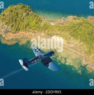 Eine Luftaufnahme eines US Marine Vought F4U Corsair Kämpfers aus dem Zweiten Weltkrieg, der über einer pazifikinsel fliegt. Stockfoto