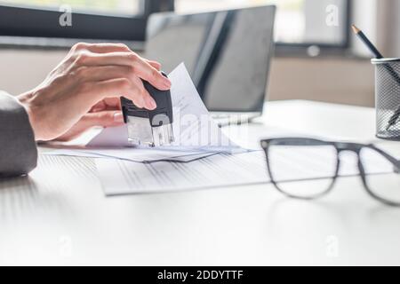 Beschnittene Ansicht der Geschäftsfrau, die am Arbeitsplatz einen Stempel in das Dokument setzt Auf unscharfem Hintergrund Stockfoto