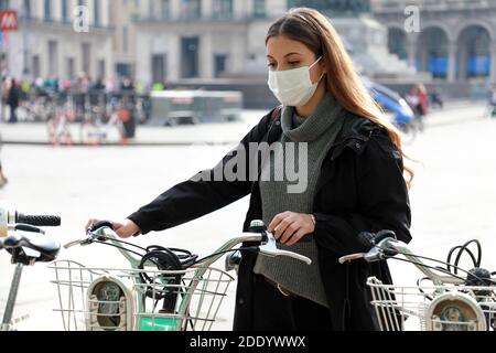 Umweltfreundlicher Transport. Geschäftsfrau mit Schutzmaske, die ein Fahrrad in einer Bike-Sharing-Plattform nimmt. Junge Frau steht in der Nähe Bike-Sharing in der Stockfoto