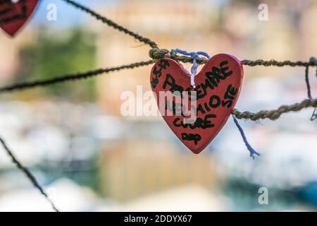 Herzform-Symbol mit italienischem Gedicht, das auf Draht-diffusem Hintergrund hängt. Für immer in meinem Herzen. Stockfoto