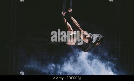 Der junge akrobat hängt in der Luft an den Seilen Stockfoto