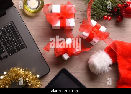 Komposition mit Geschenkpaketen auf einem Holztisch mit Weihnachtsdekorationen und digitalen Gadgets. Horizontale Zusammensetzung. Draufsicht. Stockfoto
