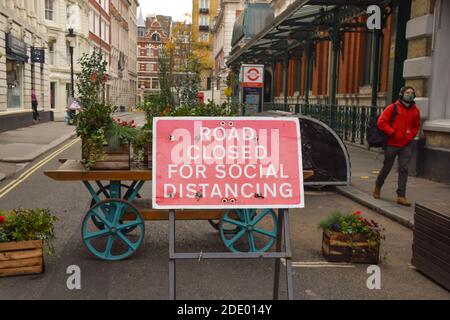 Ein Mann, der eine schützende Gesichtsmaske trägt, geht an einer Straße vorbei, die für ein soziales Distanzierungsschild in Covent Garden, London, gesperrt ist. Stockfoto