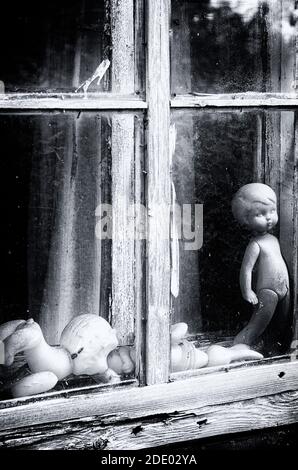 Schwarz-Weiß-Konzept Fensterrahmen mit sowjetischen Puppen ohne Markenzeichen in einem verlassenen Haus vertikale Ausrichtung (Pskov Region, Russland) Stockfoto