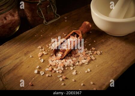 Himalayan rosa Salzkristalle in einer Holzlöffel auf einem alten Holzbrett, mit Mörtel und Stößel, England, Großbritannien, GB. Stockfoto