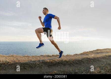 Reifer Mann Athlet laufen auf Bergpfad im Hintergrund Himmel Und Meer Stockfoto