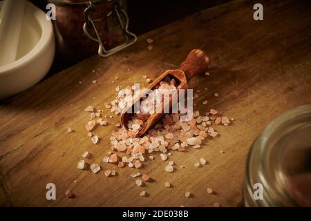 Himalayan rosa Salzkristalle in einer Holzlöffel auf einem alten Holzbrett, mit Mörtel und Stößel, England, Großbritannien, GB. Stockfoto