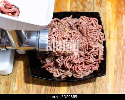 Seitenansicht des Mahlens von Hackfleisch und Zwiebeln in Elektrische Fleischwolf auf Holztisch in der heimischen Küche Stockfoto