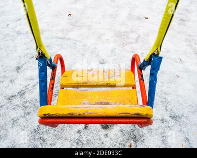 Eisbedeckte gelbe Holzschaukel auf dem Kinderspielplatz nach Glatteisregen am kalten Herbsttag Stockfoto